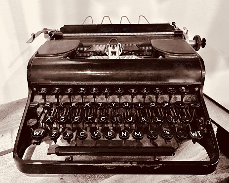 Horizontal close up still life of old fashioned antique Olympia black typewriter against white background on wood timber table top