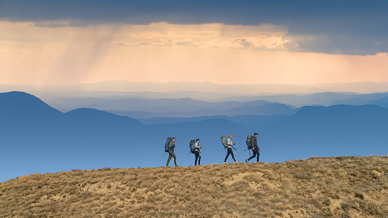 The four people with backpacks walking on picturesque mountains background