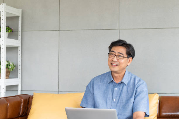 istock Asian elder senior man using computer laptop while sitting on sofa inside of the house for search and thinking about idea or information for healthcare service, lifestyle. With copy space for text. 1317119578