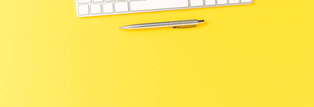 istock Elegant office desktop with computer keyboard and pen on yellow table. Business background. Top view. Banner 1317121972