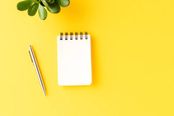 istock Office desktop with empty notebook and pen on yellow background. Business concept 1317121993
