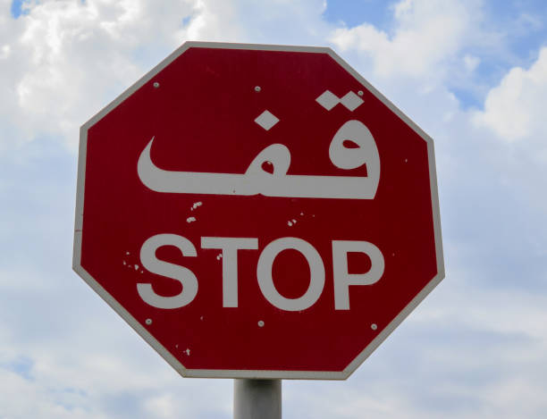 Red, octagon STOP sign in Arabic and English against an bright blue sky with white clouds