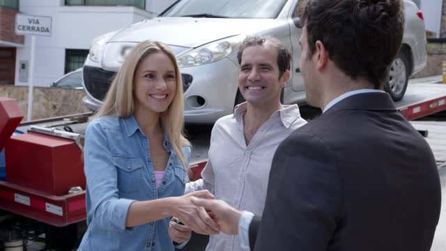 Happy couple at home receiving their car on a tow truck and salesman handing them the key while shaking hands