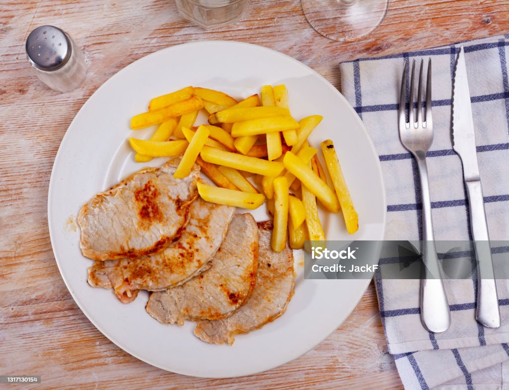 Fried barbecue pork meat with baked potato Roasted pork loin Lomo de cerdo con patata with potatoes fries on a ceramic plate cooked in a cafe Barbecue - Meal Stock Photo