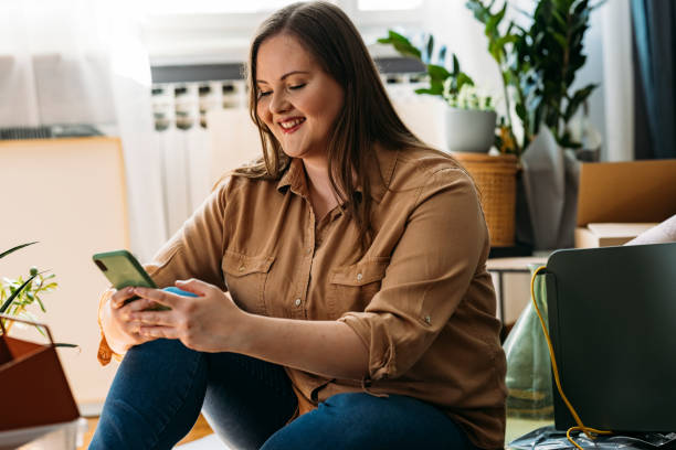 istock Moving In: Beautiful Happy Plus Size Woman Sitting on the Floor while Using a Smartphone 1317133409