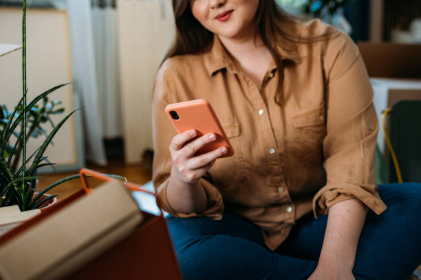 istock Moving In: Anonymous Happy Plus Size Woman Sitting on the Floor while Using a Smartphone 1317133432