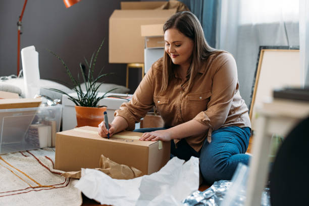 istock Moving out: Young Beautiful Plus Size Woman Sitting on the Floor while Labeling Packed up Cardboard Box (Horizontal) 1317133444