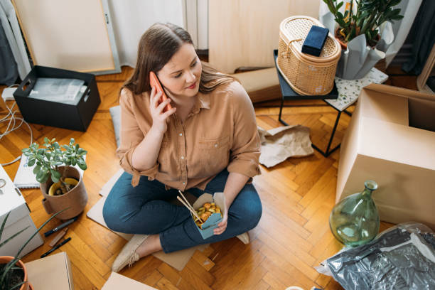 istock Moving in: Happy Plus Size Woman Sitting on the Floor and Talking on her Smartphone while Having a Lunch Break 1317133476