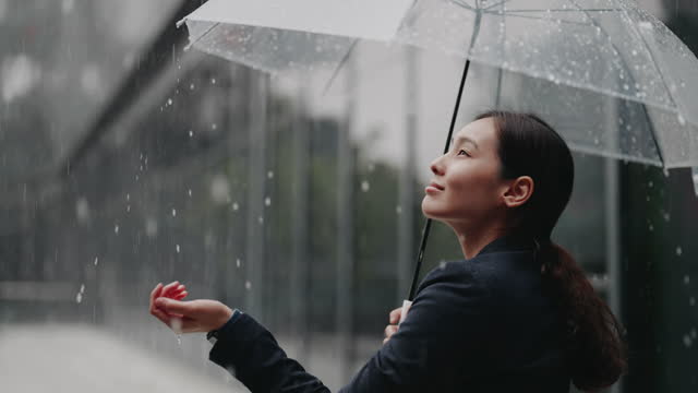Asian Businesswoman standing with umbrella in Rain