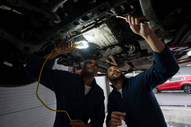 istock Mechanics working as a team at a garage fixing a car on a lift and using a lamp 1317136933