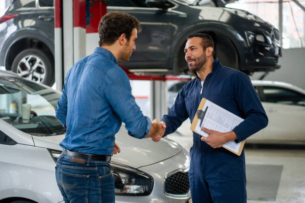 Man greeting a mechanic with a handshake at an auto repair shop Latin American man greeting a mechanic with a handshake while picking up his car at an auto repair shop repairman stock pictures, royalty-free photos & images