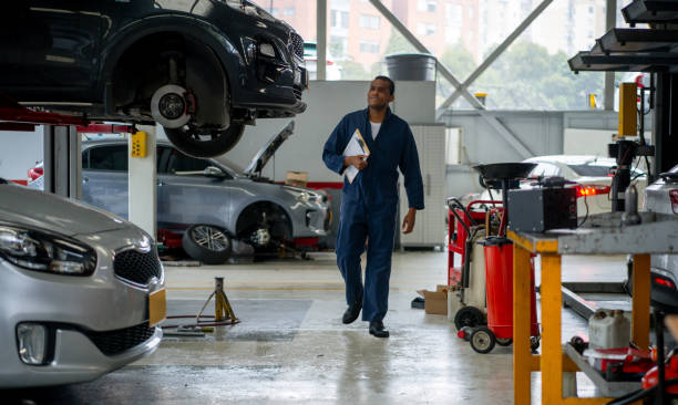 mechanic working at an auto repair shop fixing cars - full length clipboard african ethnicity black imagens e fotografias de stock