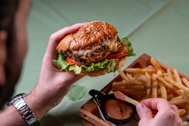 mann hält einen leckeren hamburger - ungesunde ernährung stock-fotos und bilder