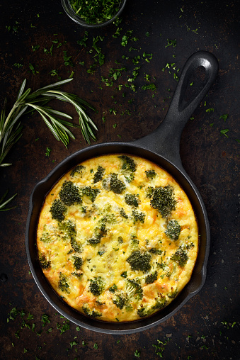 Oven baked omelet or quiche with broccoli, cheddar cheese on a dark background