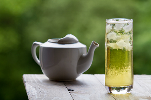 With long green ice tea and glass teapot on unfocused background
