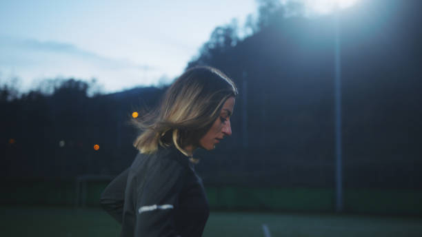 Young woman soccer player training on grass field at night.