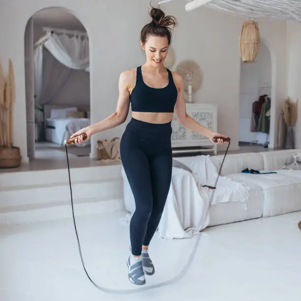 Girl exercising with jumping rope at home. Fit woman skipping rope