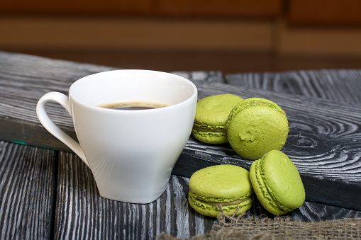 Light green macarons lie on a saucer. Nearby is a cup of coffee.