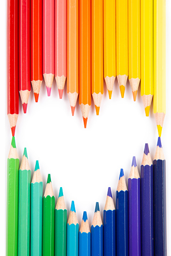 Top view of vibrant rainbow colored pencils arranged in heart shape on white background with useful copy space.