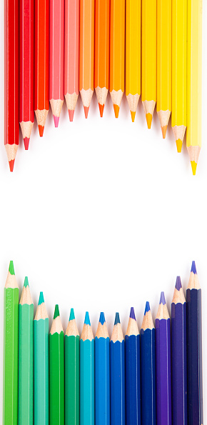 Top view of vibrant rainbow colored pencils arranged in circle shape on white background with useful copy space.