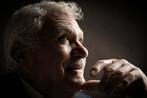 A portrait of 60-70 years old serious thoughtful mature man.  He has put his thump on his chin and he is looking up.  The photo was shoot indoors by window with daylight.