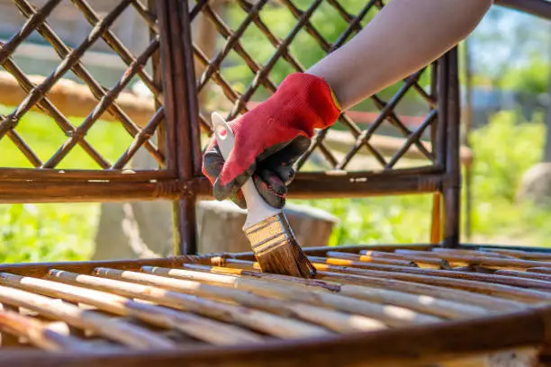 Young girl painting wooden exotic wood bench in the garden with a brush. Close up