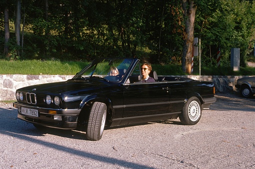 Around Munich, Bavaria, Germany, 1984. A young urban professional (yuppie) couple in their black BMW convertible on a weekend trip.