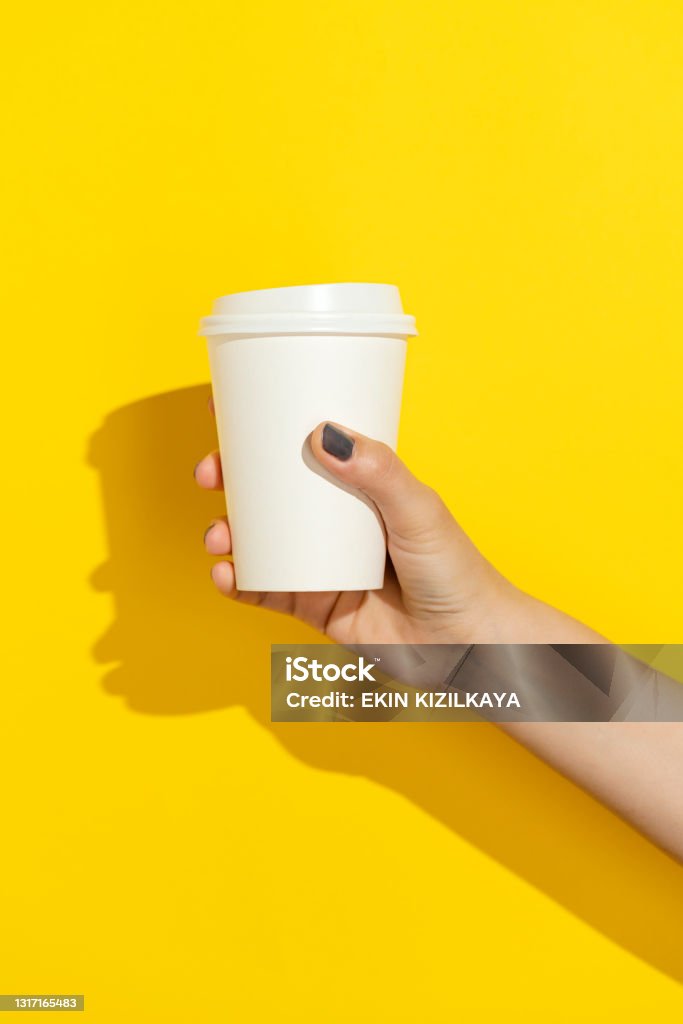 Hand holding white disposable paper cup Hand holding disposable paper cup with plastic lid on yellow background Coffee - Drink Stock Photo