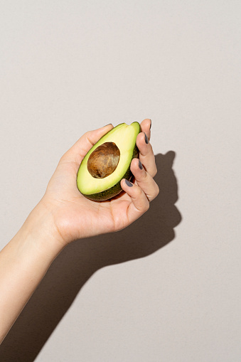 Hand holding half avocado on white background