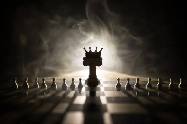 Photo of chess board game concept of business ideas and competition and strategy ideas concep. Chess figures on a dark background with smoke and fog and window with sunlight. Selective focus