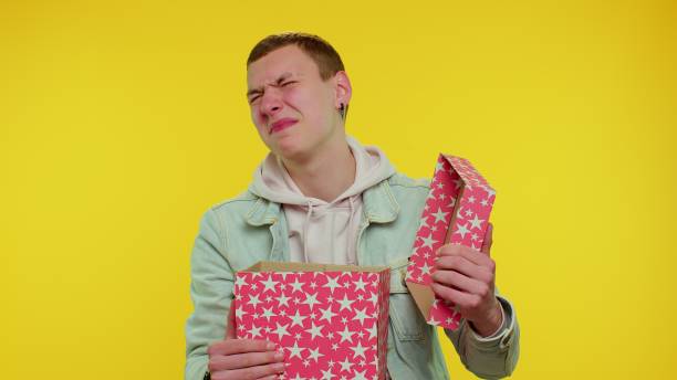 istock Young man unwrapping birthday gift and expressing disappointment, dislike bad present, dissatisfied 1317177554