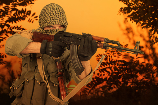 guerilla fighter firing AK 47 gun in jungle forest. Sunset background.