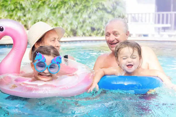 Portrait of great-grandparents with great-grandchildren on vacation. Active retirees play with children in the pool
