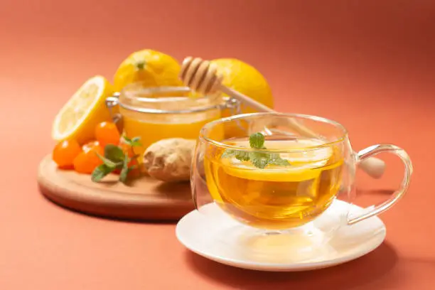 Ginger tea with mint and lemon. Healthy and hot drink. Liquid honey in honey-jar. Crystal cup on bright background. Selective focus. High quality photo