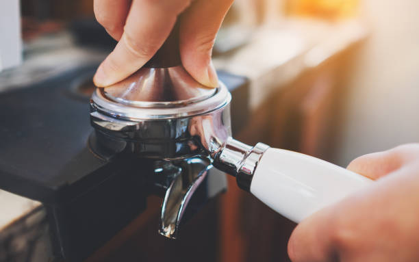 barista utilisant une altération pour presser le café moulu dans un portafilter dans le café - tamping photos et images de collection