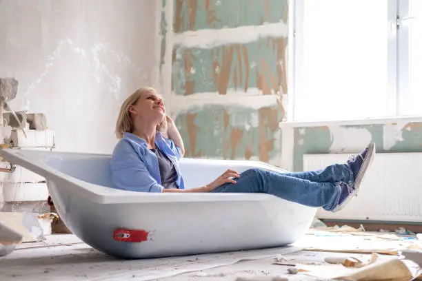Renovation apartment. Creative story young dreaming plan woman sits in bathtub in the middle of the room. Empty walls, repairs house with their own hands.