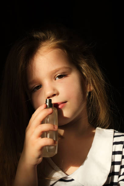 istock Beautiful little girl sniffs perfume from a bottle, in dark settings 1317200869