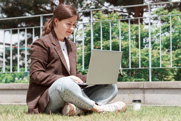 istock Young woman sitting on the grass and typing on laptop side view. 1317200925