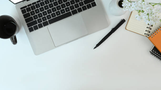 istock Top view of simple workspace with laptop computer, glasses, notebook, coffee cup and plant on white desk. 1317211491
