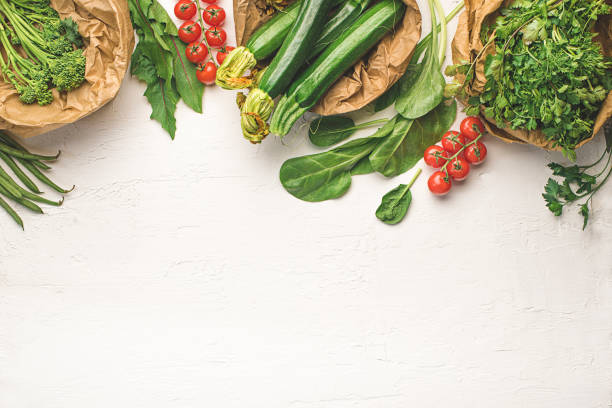 From garden to table. Various fresh vegetables and green ingredients on white table background, top view, frame, zero waste, green eating layout