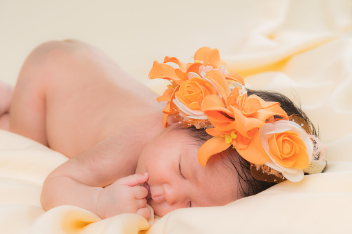 Portrait of a one month old sleeping, newborn baby girl. She is wearing a flower crown and sleeping on a cream blanket. Concept portrait studio fashion newborn.