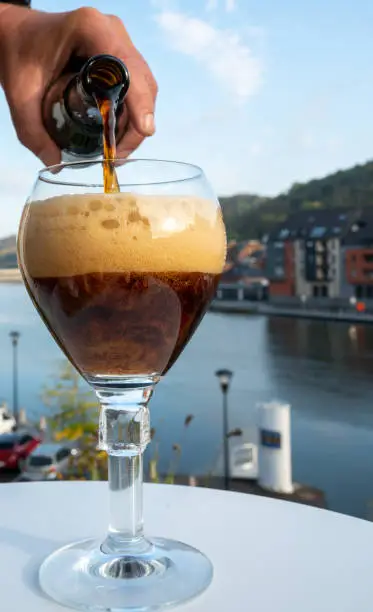 Pouring of strong Belgian abbey beer and tasting of cheeses made with trappist beer and fine herbs with view on Maas river in Dinant, Wallonia, Belgium