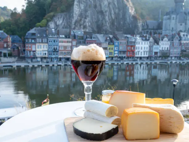 Glass of strong Belgian abbey beer and tasting of cheeses made with trappist beer and fine herbs with view on Maas river in Dinant, Wallonia, Belgium