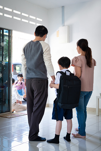 Asian Chinese parents get ready to send their boy and girl on the first day of school. While grandmother helping granddaughter to wear school shoes at door entrance. Family, Love & Parenthood, Youth Education and Learning, Back to School Concepts.