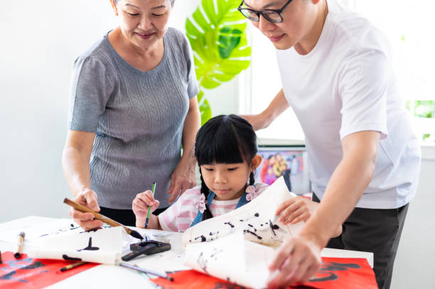 asiatische großmutter führt und lehrt ihre enkelin die richtige art und weise, traditionelle chinesische kalligraphie im wohnzimmer zu schreiben - chinese script text calligraphy grandmother stock-fotos und bilder
