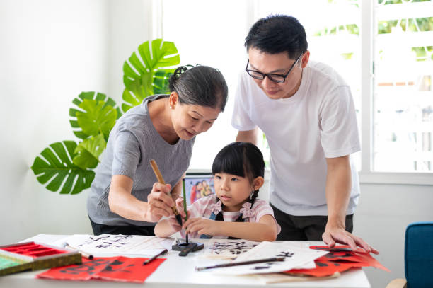 asian grandmother guiding and teaching her grand daughter the proper way of holding calligraphy brush to write good traditional chinese calligraphy. - chinese script text calligraphy grandmother imagens e fotografias de stock