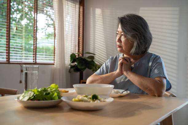 asian anziana nonna in pensione stare a casa con il viso doloroso seduto da solo sul tavolo da mangiare in casa. depressa matura anziana anziana sconvolta sentendosi infelice, sola e mancando la sua famiglia a casa. - senior women depression sadness women foto e immagini stock