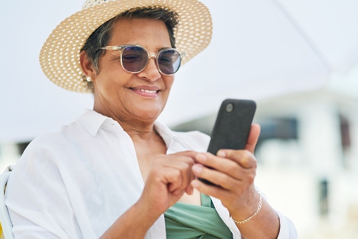 istock Shot of a mature woman sitting alone and using her cellphone during a day out on the beach 1317237556