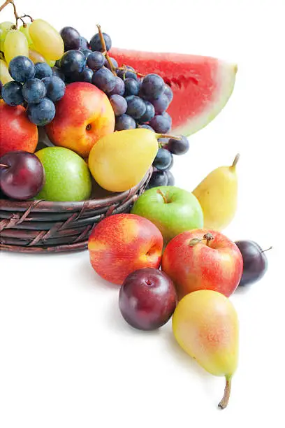Various fresh ripe fruits placed in a wicker basket and around on white background.