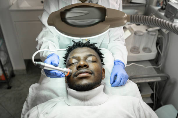 A male customer receiving a facial treatment under a bright light A male customer receiving a facial treatment by the clinician wearing protective gloves, under a bright light black male massage stock pictures, royalty-free photos & images